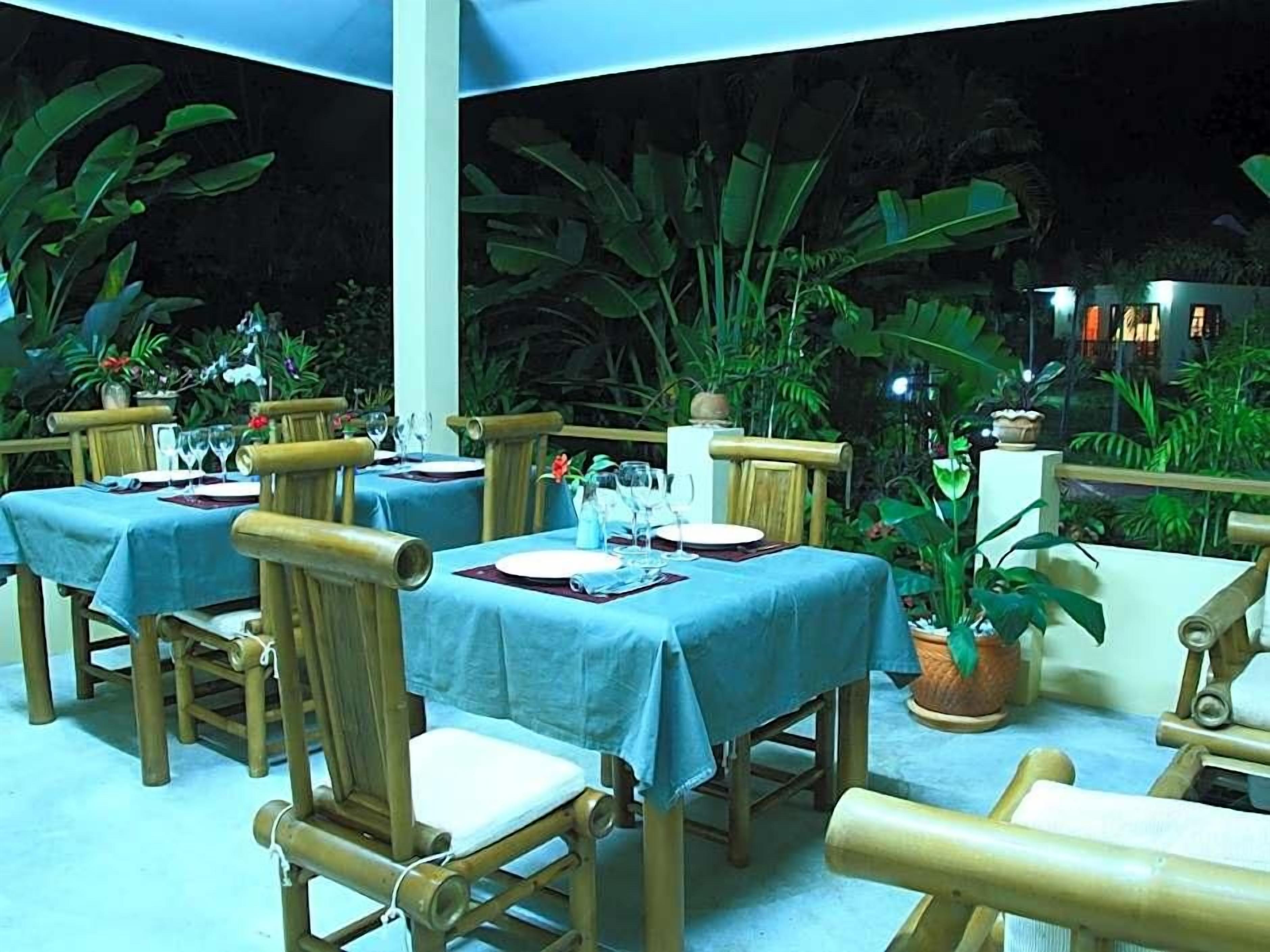 An outdoor dining area with tables set for two, surrounded by lush greenery.