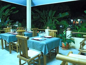 An outdoor dining area with tables set for two, surrounded by lush greenery. - Mai Siam Resort (Mae On)