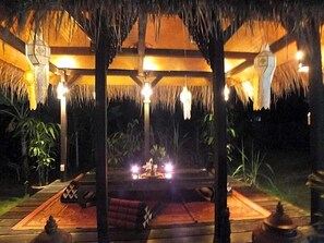 An outdoor seating area with thatched roof, wooden furniture, and ambient lighting. - Mai Siam Resort (Mae On)