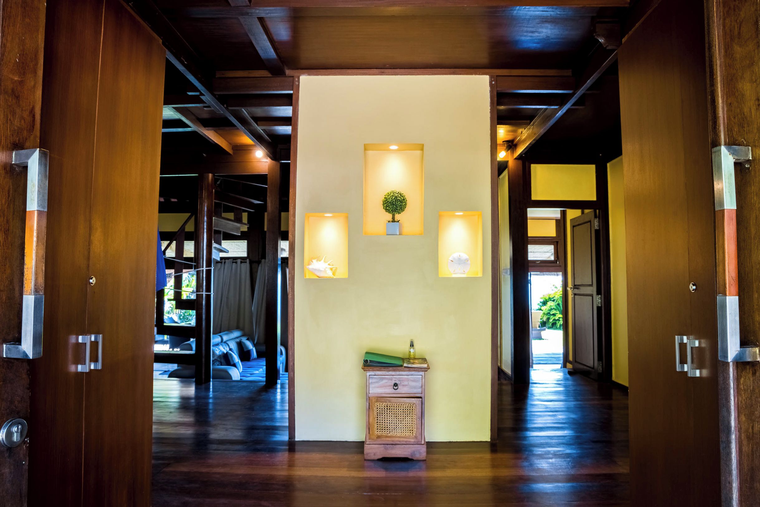 Un couloir avec des portes en bois, un petit meuble en bois et des lampes fixées au mur.