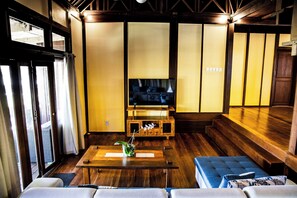 A traditional Japanese-style living room with tatami flooring, a low wooden coffee table, a sofa, and a television set.