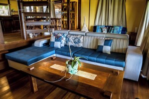A modern living room with a sectional sofa, wooden coffee table, and a bookshelf. - Bora Bora waterfront sunrise villa (Bora Bora)
