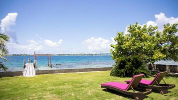 A grassy area with two lounge chairs and a tree, overlooking a body of water with a dock and a pier.