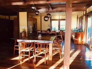 A spacious dining area with a long wooden table and chairs, a kitchen in the background, and large windows allowing natural light. - Bora Bora waterfront sunrise villa (Bora Bora)