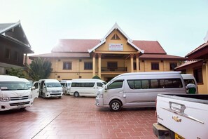 A parking area with several white vehicles, a building with a red roof, and a sign indicating 'Muttaphap Hotel 2'. - Mittaphap Ii Hotel (Luang Prabang)