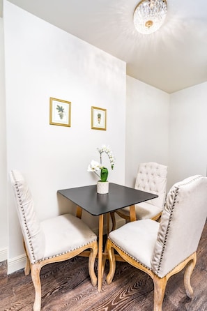 A corner room with a dark wooden table, two upholstered chairs with decorative stitching, and two framed botanical prints on the wall. - Spacious 1BD | Elegant Condo Near Bourbon St (New Orleans)