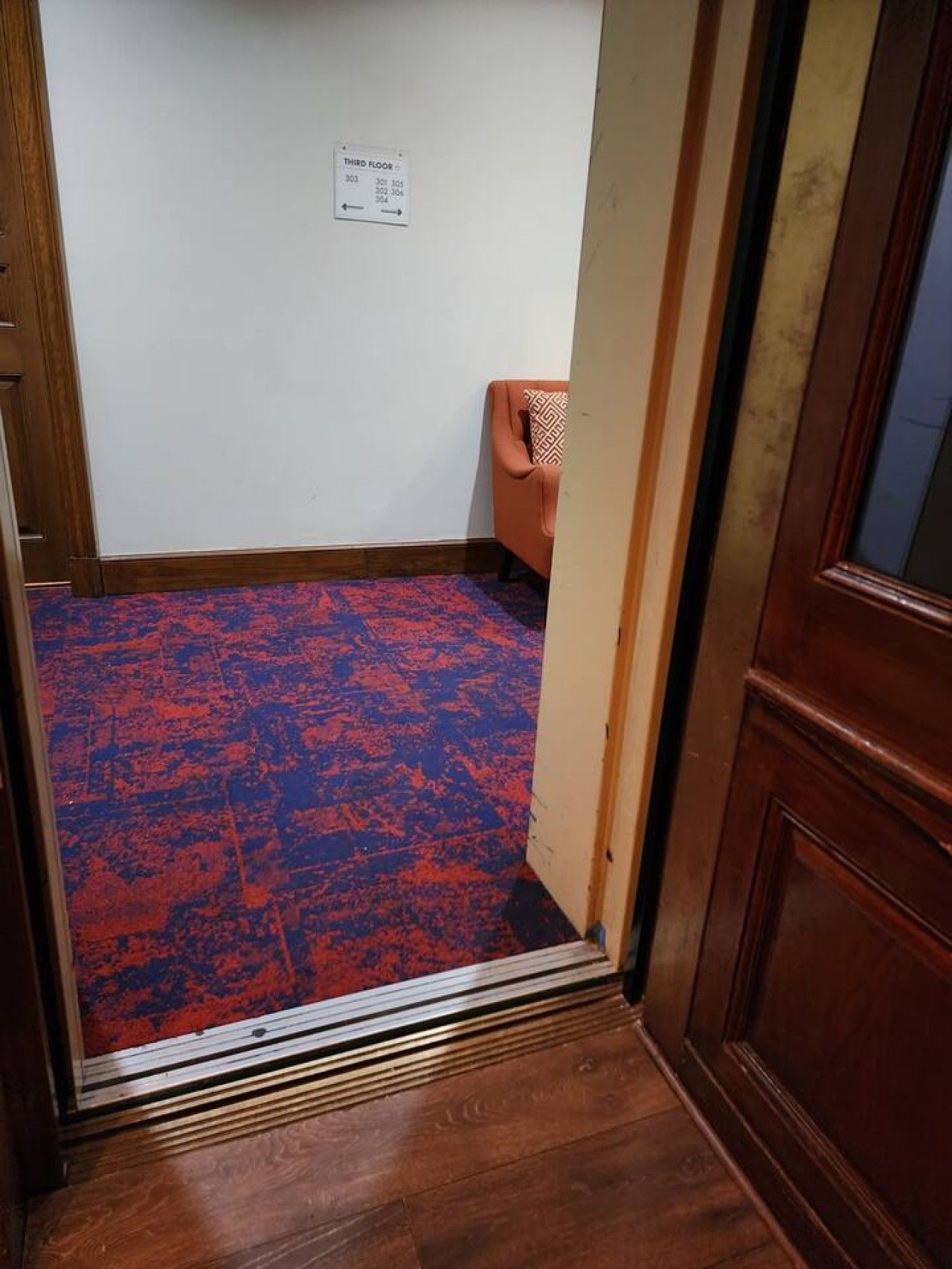 A room with a patterned carpet, a wooden door, and a wall-mounted electrical outlet.