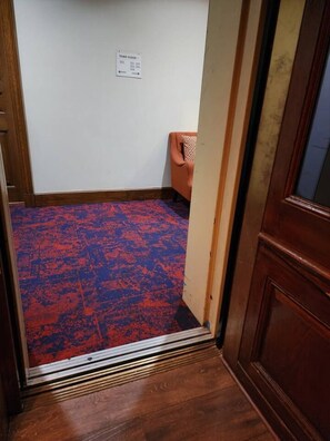 A room with a patterned carpet, a wooden door, and a wall-mounted electrical outlet. - Spacious 1BD | Elegant Condo Near Bourbon St (New Orleans)