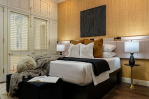 Une chambre à coucher avec un lit, des lampes de chevet, une tête de lit et une œuvre d’art accrochée au mur.