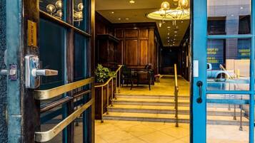 L’entrée d’un hôtel, avec une porte en bois, un paillasson accueillant et un escalier menant à un hall d’accueil.
