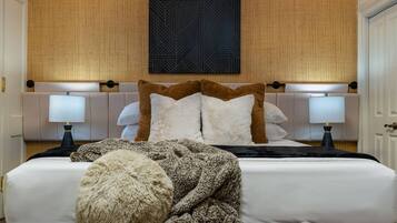 A hotel room with a large bed, two bedside tables with lamps, a headboard with a geometric pattern, and a fluffy throw blanket on the bed.