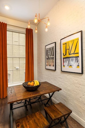 A dining area with a wooden table, two chairs, a fruit bowl, and a wall-mounted light fixture. - Modern 2BD in CBD | Walk to Bourbon St (New Orleans)