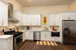 A modern kitchen with white cabinetry, stainless steel appliances, and a striped rug. - Modern 2BD in CBD | Walk to Bourbon St (New Orleans)