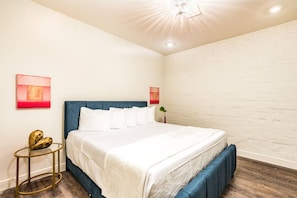 A bedroom with a bed, a round gold table, and a wall-mounted light fixture. - Modern 2BD in CBD | Walk to Bourbon St (New Orleans)