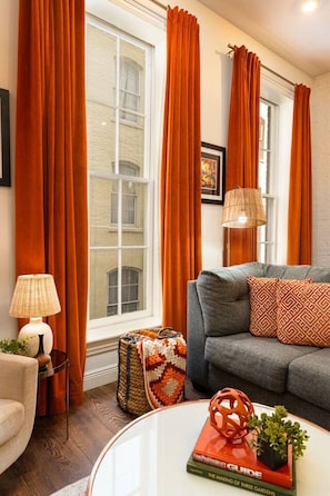A living room with a sofa, a coffee table, a lamp, and a book titled 'The Making of Three Gardens'. - Modern 2BD in CBD | Walk to Bourbon St (New Orleans)