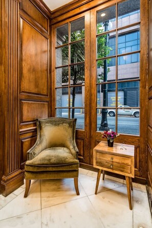 A corner room with a wooden paneled wall, a plush armchair, a small wooden side table with a vase, and a large window with a view of the street. - Modern 2BD in CBD | Walk to Bourbon St (New Orleans)