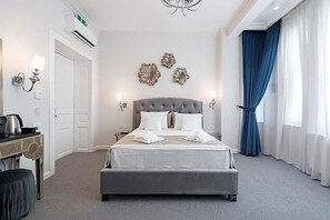 A hotel room with a large bed, bedside lamps, decorative wall art, a desk with a kettle, and a blue curtain. - Highline Downtown Old Town Unirii Square (Bucharest)
