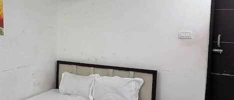 Una cama individual con colchón y almohadas blancas, un aire acondicionado de pared y una puerta cerrada.