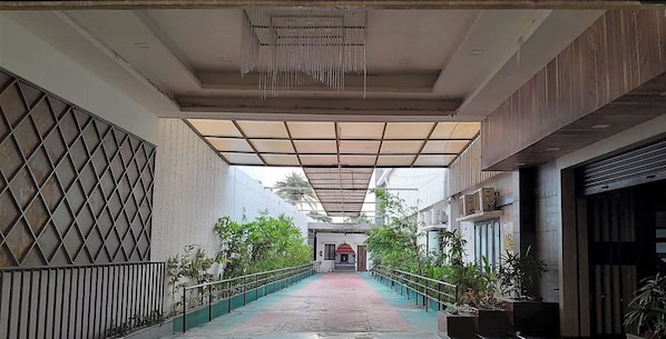 A corridor with a tiled ceiling, a metal railing, and potted plants.