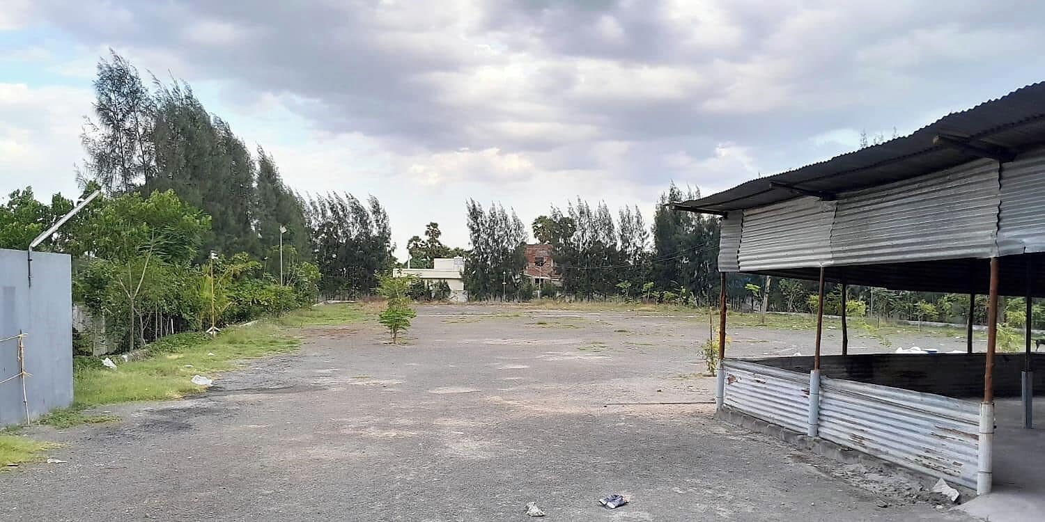 A parking area with a small tree, a corrugated metal structure, and a building in the background.