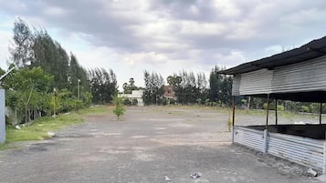 A parking area with a small tree, a corrugated metal structure, and a building in the background.
