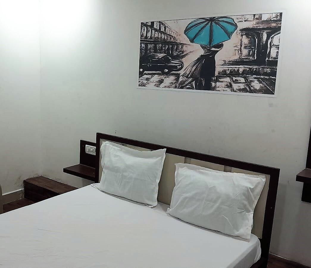 A bed with white bedding, two pillows, and a headboard in a room with a wall-mounted painting.