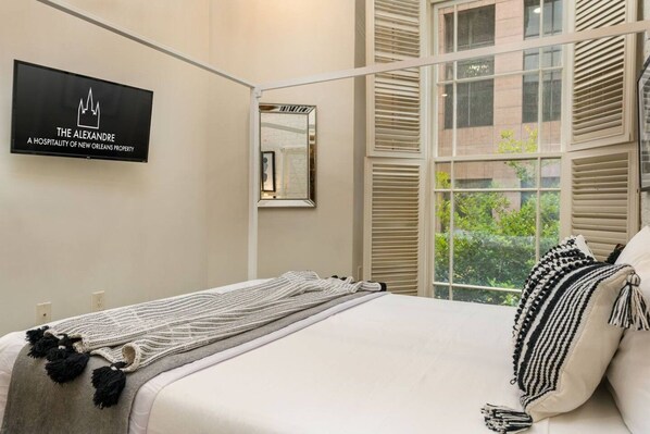 A hotel room with a bed, a framed picture, a window with blinds, and a sign on the wall. - Stylish NOLA 2BD | Steps from French Quarter (New Orleans)