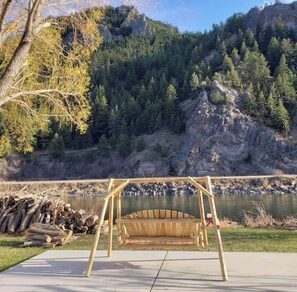 Una silla mecedora de madera en un parque con vista a un río y montañas.