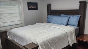 A bedroom with a wooden bed, a nightstand, a window with blinds, and a picture on the wall. - River Cabin is in Cascade right on the Missouri River (Cascade)