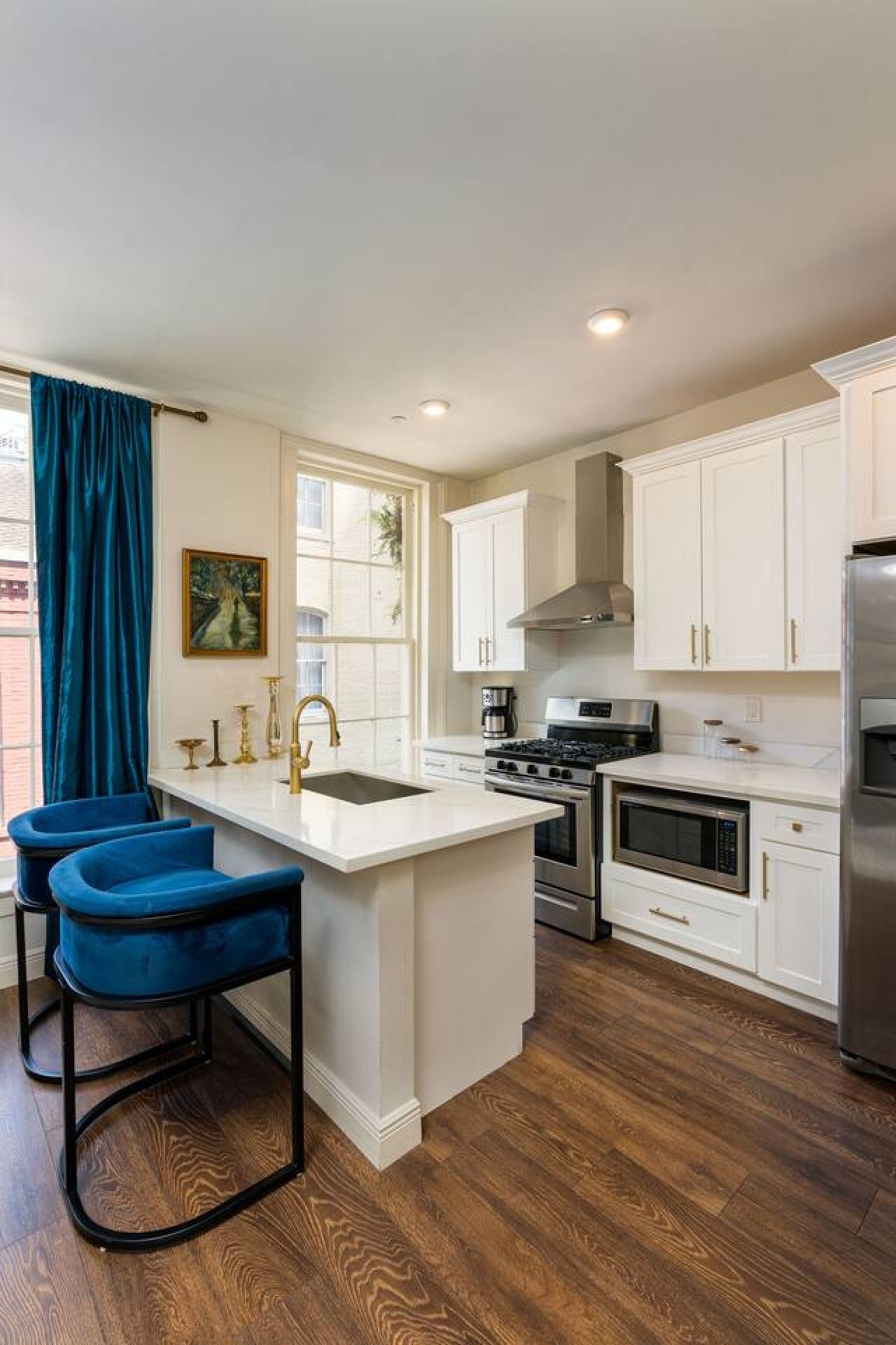 A modern kitchen with white cabinetry, a central island, and blue bar stools.