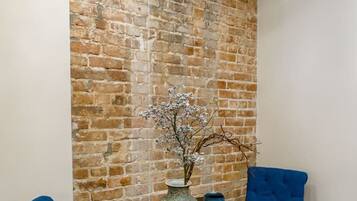 Un coin repas avec un mur en briques, un vase de fleurs et des chaises recouvertes d’un tissu bleu.