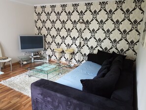 Un salon moderne avec un téléviseur à écran plat, une table basse en verre, un canapé et un papier peint à motifs.