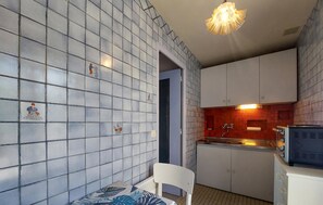 Eine kompakte Küche mit weißen Schränken, einer gefliesten Spritzschutzwand und einer kleinen Essecke mit einem Stuhl.
