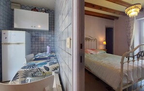 Ein Zimmer mit einem Bett, einem Schreibtisch mit Stuhl, einem Kühlschrank und einem Wasserkocher.