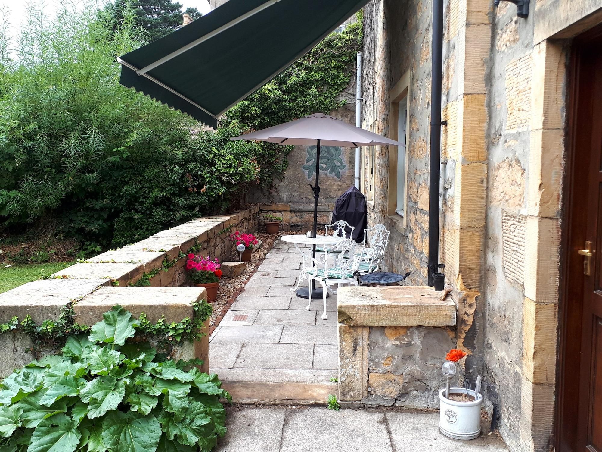 An outdoor patio with a table and chairs, a potted plant, and a stone wall.