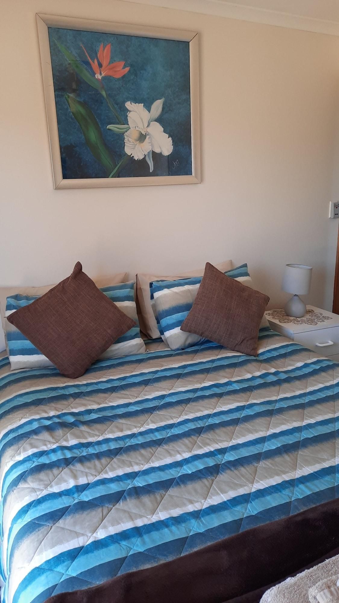 A bed with striped bedding, a painting of flowers on the wall, and a bedside table with a lamp.