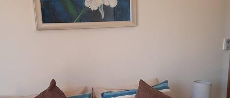 A bed with striped bedding, a painting of flowers on the wall, and a bedside table with a lamp.