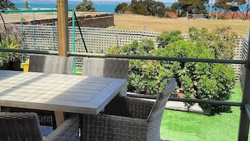 A covered outdoor seating area with a table and chairs, overlooking a landscaped garden and a body of water.