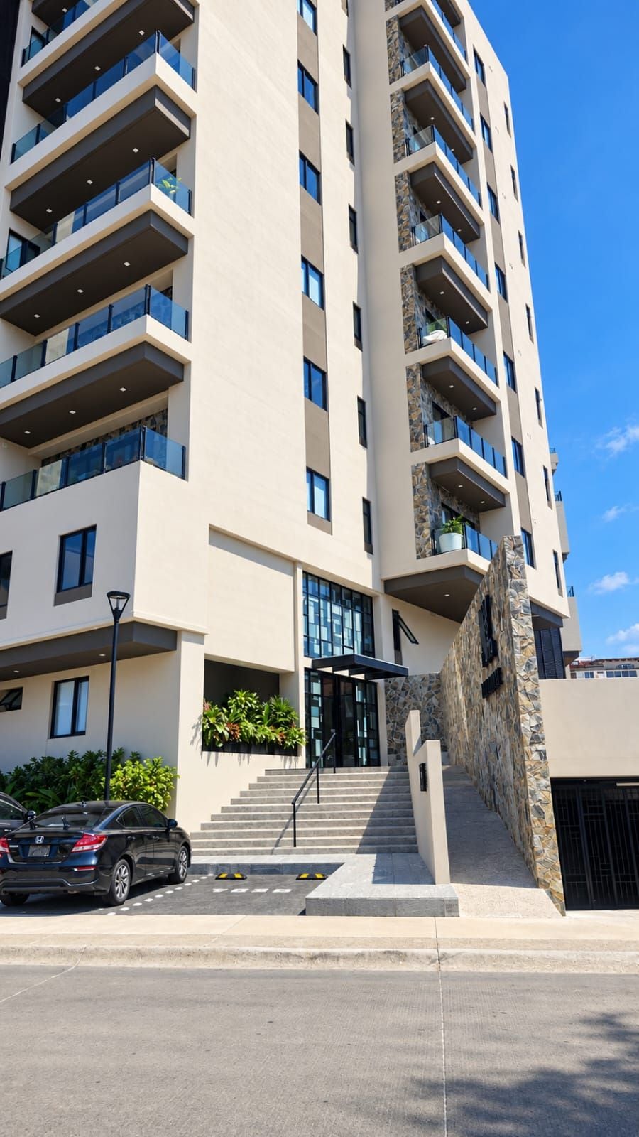 A multi-story hotel with a modern design, featuring balconies, a stone facade, and a clear sky.