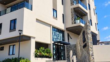A multi-story hotel with a modern design, featuring balconies, a stone facade, and a clear sky.