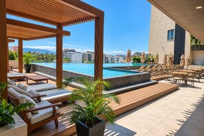 Zona de piscina en la azotea con sillones, sombrillas y vistas al paisaje urbano.