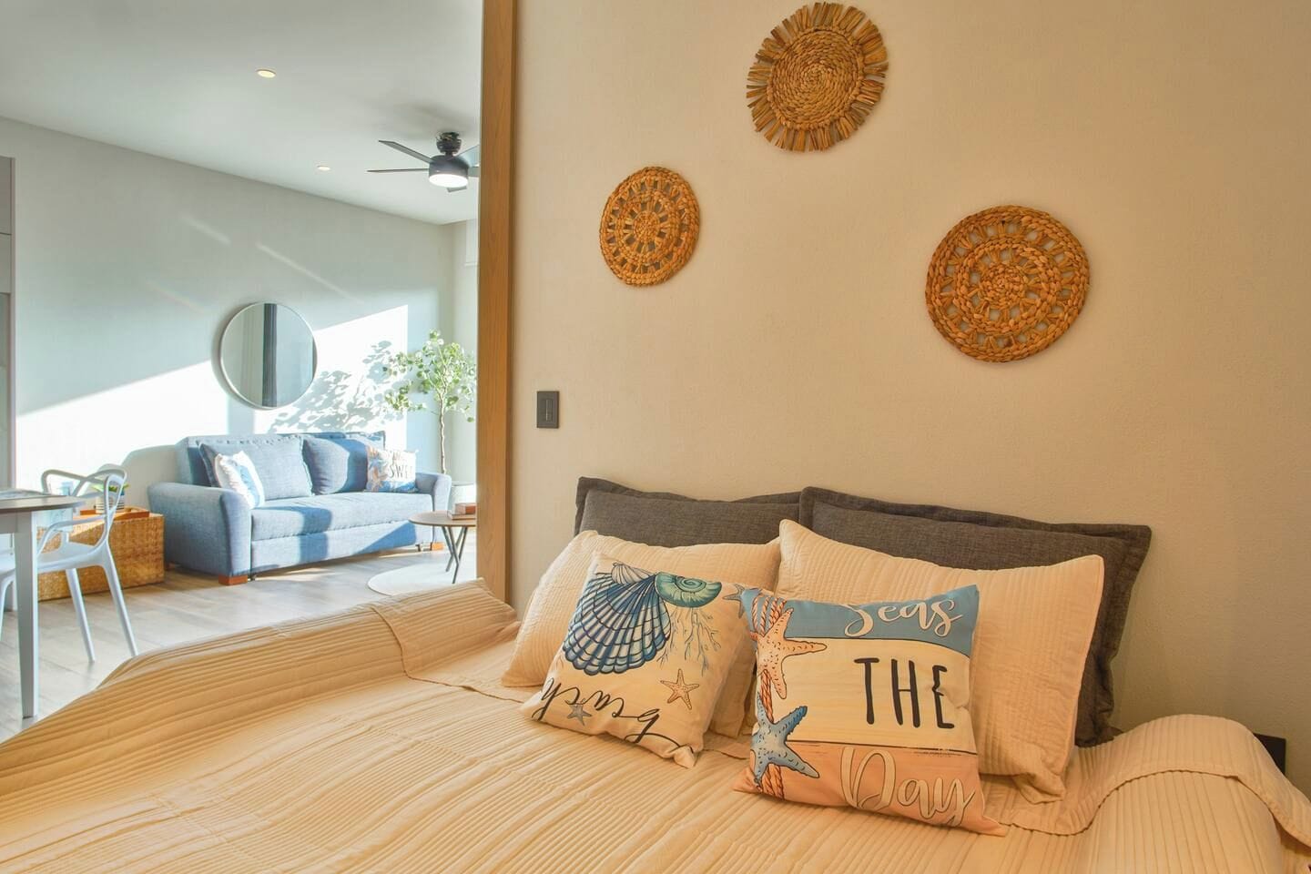 A modern bedroom with a large bed, two wall-mounted decorative items, and a view of a living area with a sofa and a dining table.