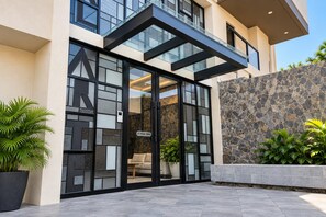 A modern building entrance with a glass door, a stone wall, and potted plants. - Versalles Lovely Condo • Pool, Cinema & Coworking (Puerto Vallarta)