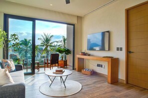 Ein modernes Wohnzimmer mit großem Fernseher, einer Couch, einem Couchtisch und einem Balkon mit Blick auf Palmen.