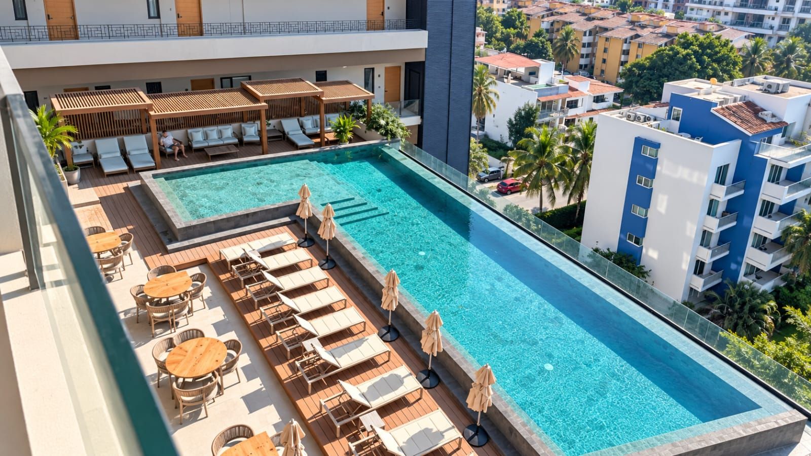 Ein Poolbereich auf dem Dach mit Liegestühlen und Sonnenschirmen, umgeben von Gebäuden und Palmen.