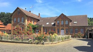 Ein traditionelles Backsteingebäude mit symmetrischer Fassade, einem zentralen Eingang und einem kleinen Garten mit Blumen.