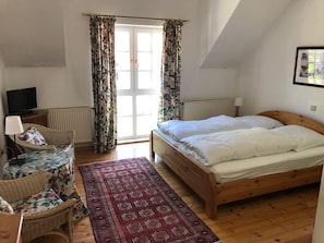 A bedroom with a wooden bed, a chair, a television, and a window with curtains. - Gutshof Eucken (Algermissen)