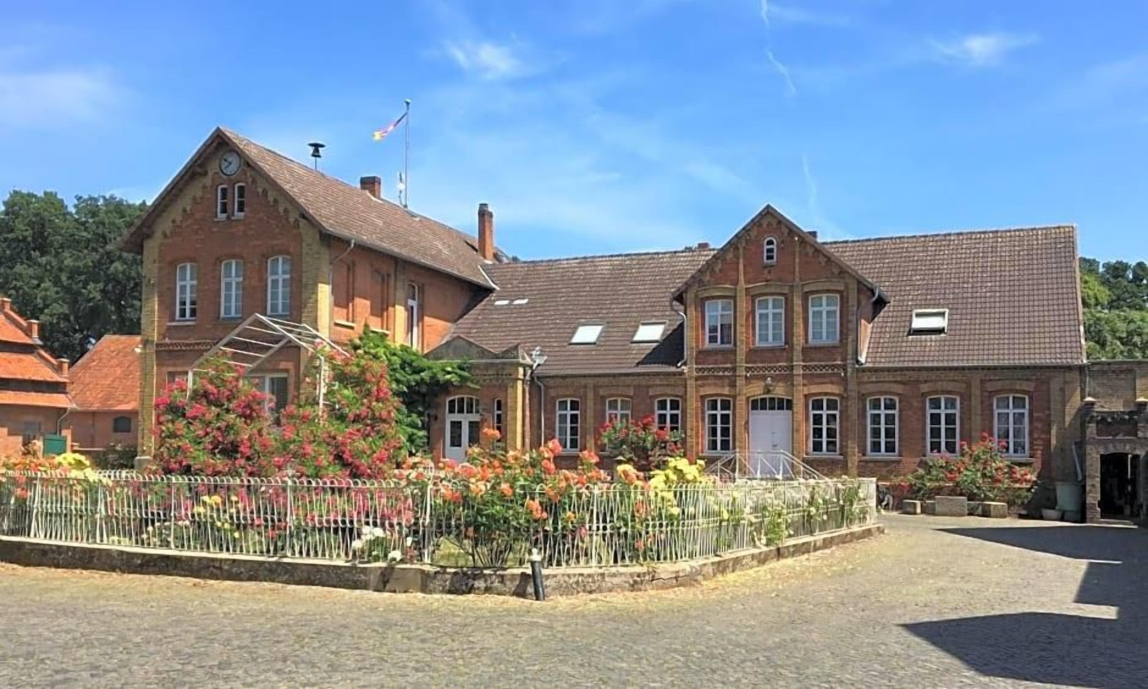 Ein traditionelles Backsteingebäude mit symmetrischer Fassade, einem zentralen Eingang und einem kleinen Garten mit Blumen.