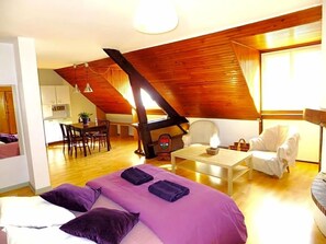 A bedroom with a sloped ceiling, a bed with purple bedding, a white chair, a small table, and a desk area with a chair. - Hv¥tel Les Templiers (Luz-Saint-Sauveur)