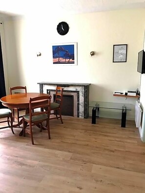 Quarto com mesa de jantar de madeira, cadeiras, lareira, relógio e quadros na parede.